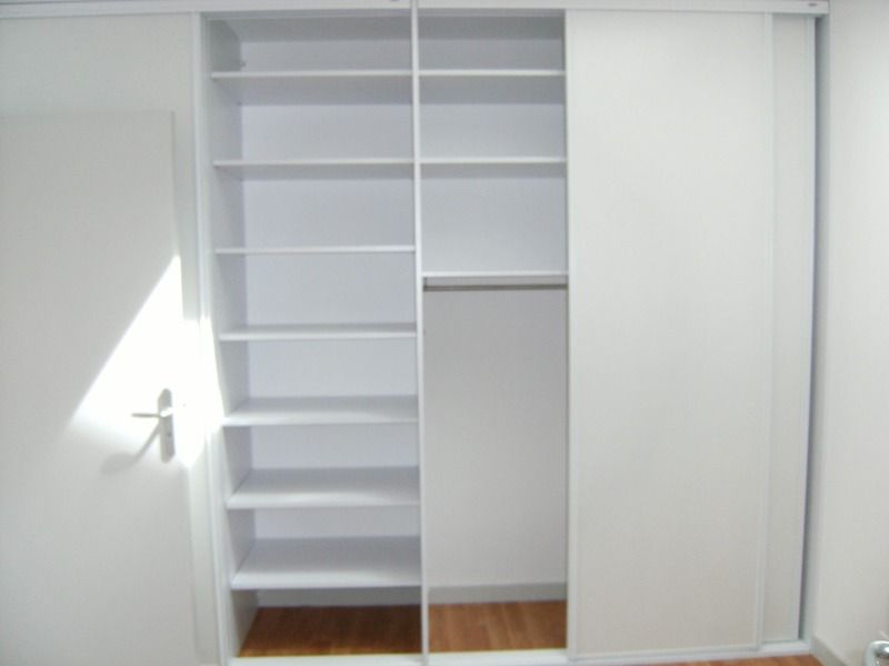 Dressing blanc avec étagères, tringles et portes coulissantes.