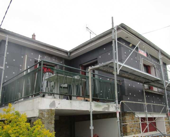 Maison à deux étages en rénovation avec échafaudages gris et rambarde de balcon
