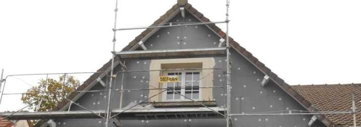 Pignon de maison grise avec échafaudage sur le toit et petite fenêtre centrale