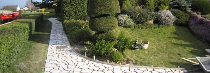 Jardin paysager soigné avec un chemin de pierre, des haies taillées et des arbustes topiaires arrondis baignés de soleil.