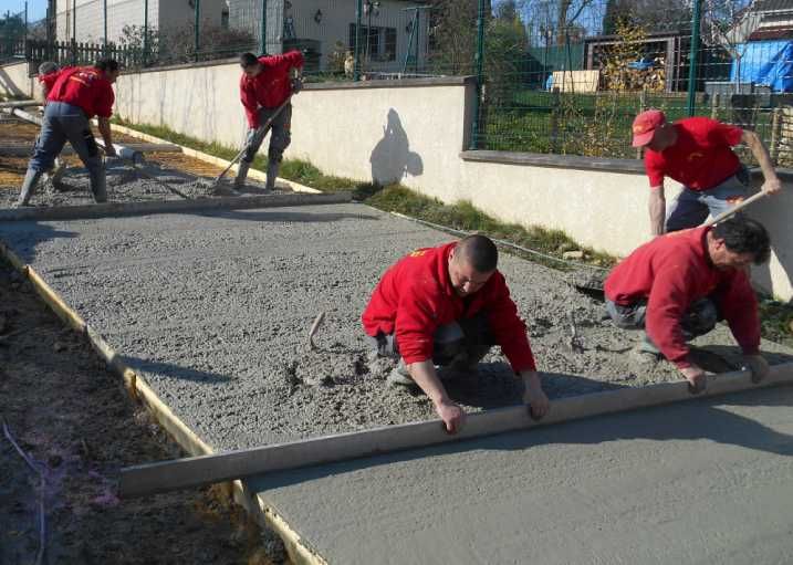 Des ouvriers en chemises rouges lissent du béton frais sur un chantier.