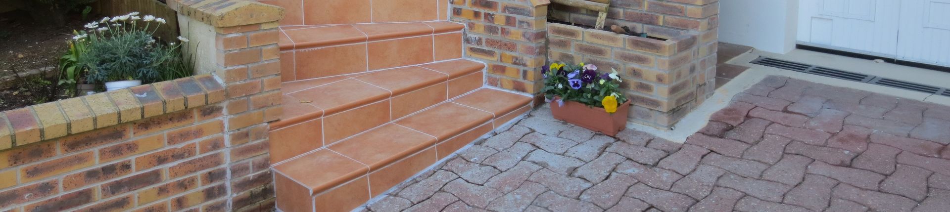 Marches et palier en briques avec des fleurs en pot à côté d'une allée pavée et d'un mur en briques.