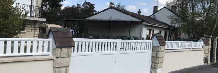 Clôture et portail blancs devant une maison de plain-pied au toit gris et aux piliers en briques.