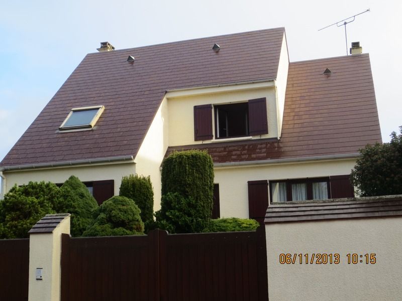Maison individuelle avec toit marron, murs couleur crème et portail d'entrée, vue depuis la rue.