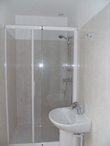 Petite salle de bains carrelée avec cabine de douche en verre et lavabo blanc.