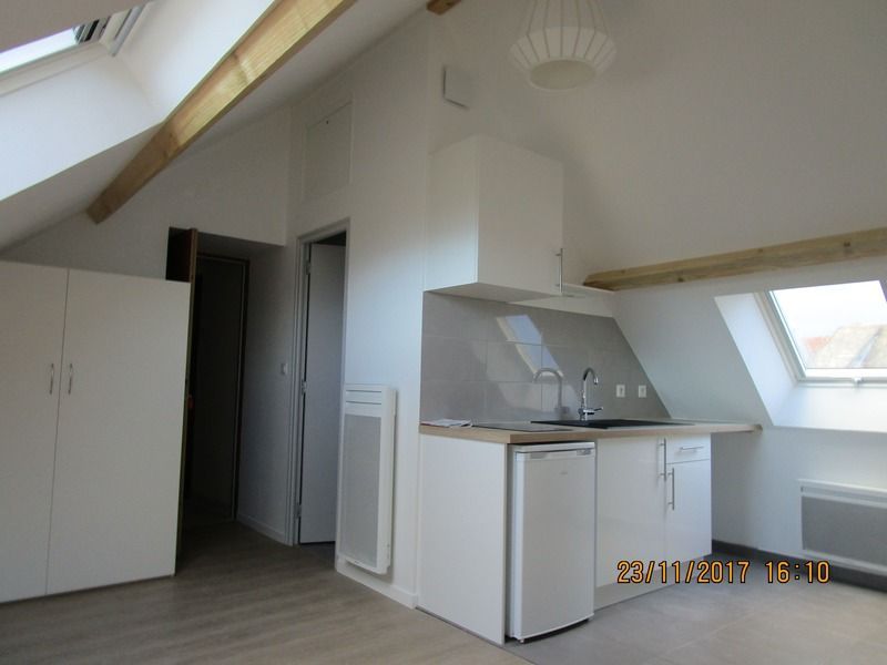 Cuisine mansardée lumineuse avec placards blancs, sol gris, puits de lumière et plafond en pente.