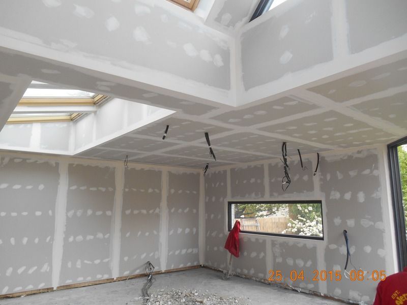 Pièce inachevée avec cloisons sèches, câblage apparent au plafond et une petite fenêtre laissant entrer la lumière du jour.