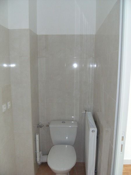 Petite salle de bains avec toilettes blanches et radiateur à côté de murs carrelés beiges.