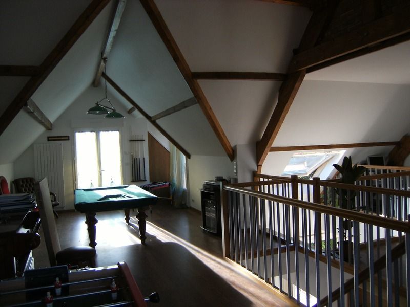 Salle de jeux sous les combles avec table de billard, poutres apparentes et lumière naturelle grâce aux fenêtres