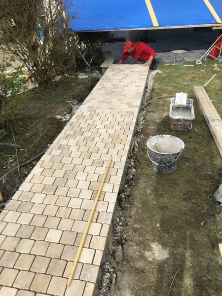 Un ouvrier pose des pavés beiges pour faire une allée.