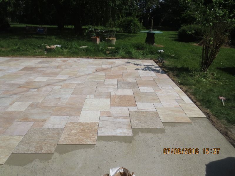 Terrasse en pierre avec des carreaux irréguliers de couleur crème, jouxtant un jardin gazonné.