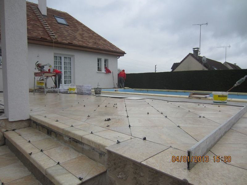 Terrasse en construction à côté d'une maison, avec marches carrelées et outils de jardin par temps nuageux
