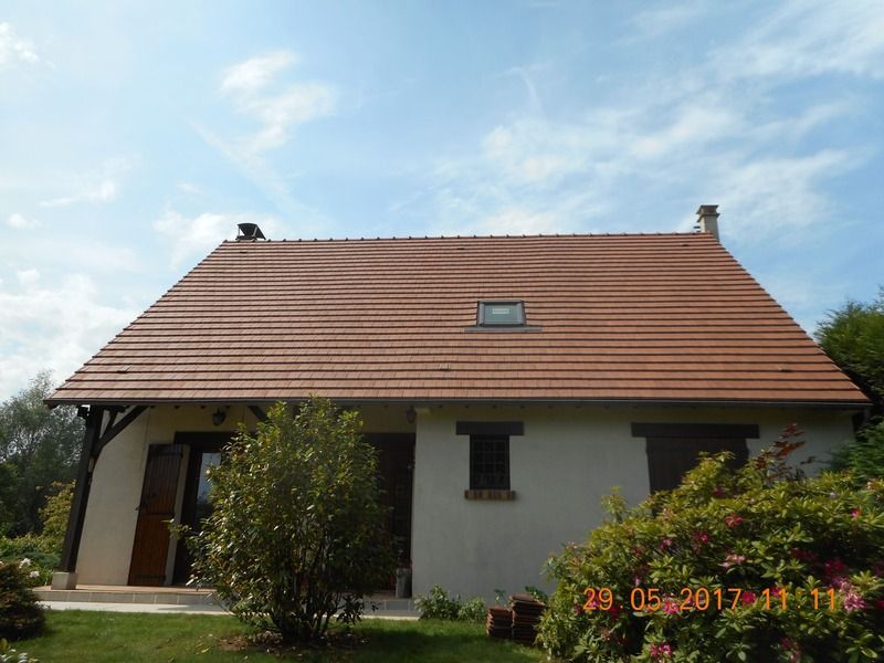 Petite maison blanche au toit pentu de tuiles rouges, vue de face sous un ciel bleu.