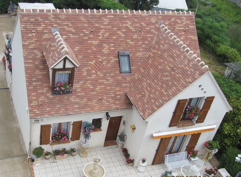 Vue aérienne d'une petite maison blanche au toit de tuiles rouges et aux jardinières près des fenêtres