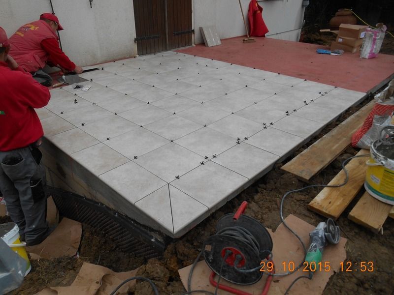 Des ouvriers installent des carreaux de sol blancs sur une plateforme intérieure surélevée.