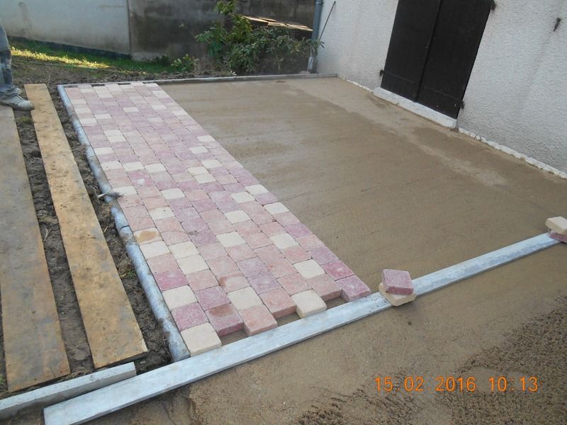Cour nouvellement pavée avec une zone en béton beige, une bande de pavés roses et une bordure blanche.