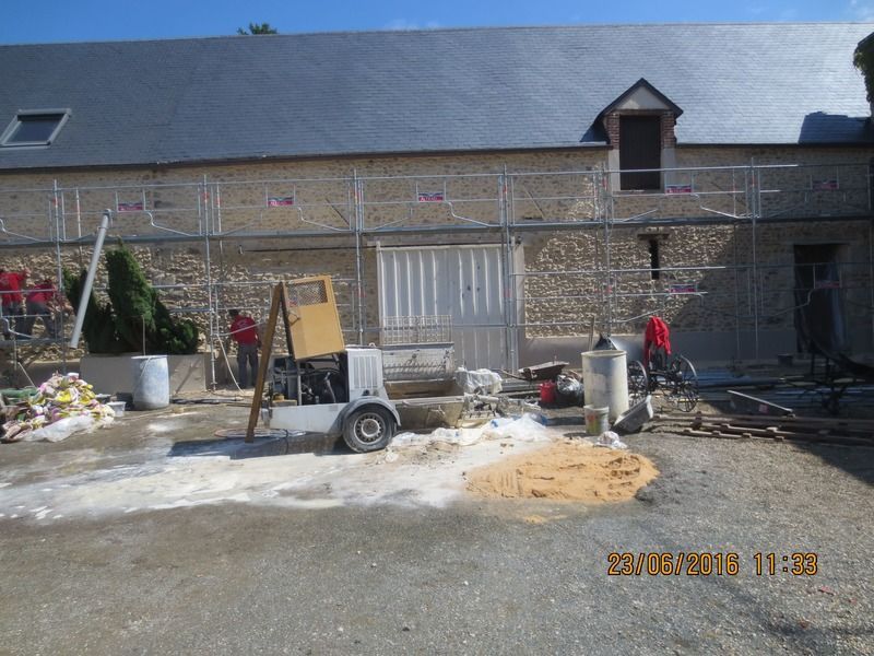 Cour intérieure d'un bâtiment en pierre avec du matériel de construction, des ouvriers et des matériaux éparpillés sous un toit gris
