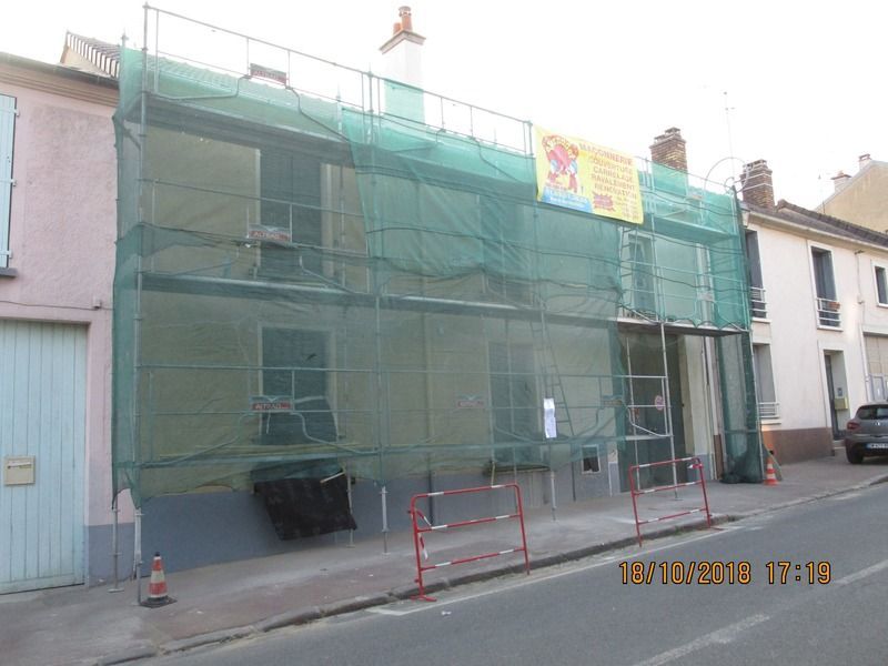 Façade d'immeuble recouverte de filets d'échafaudage verts et travaux de rénovation dans une rue étroite