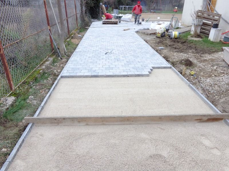 Allée extérieure en construction avec des dalles de béton et des ouvriers au loin