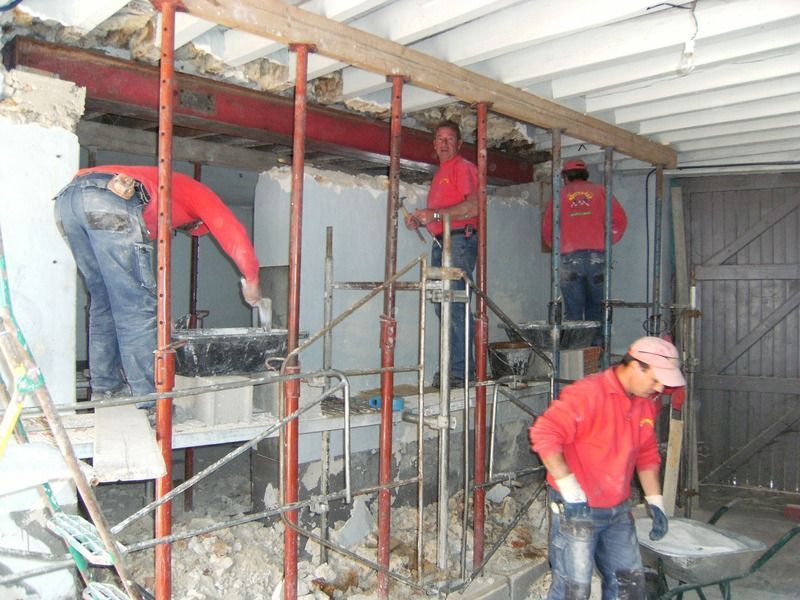 Des ouvriers du bâtiment installent des échafaudages à l'intérieur d'un bâtiment partiellement achevé, aux murs blancs et au toit métallique.