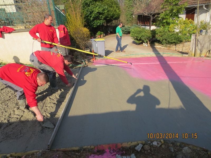 Des ouvriers lissent le béton frais d'une allée avec des outils à long manche