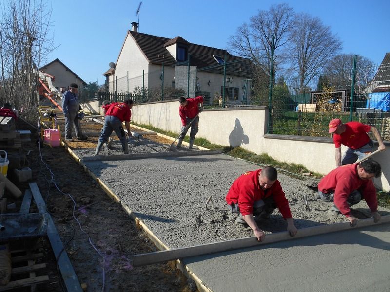 Des ouvriers en chemises rouges nivellent du béton frais sur une allée d'un chantier de construction de maison