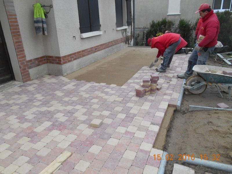 Des ouvriers posent des carreaux roses et beiges dans une cour près d'une maison.