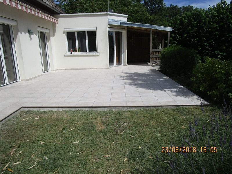 Vue sur la terrasse et le jardin d'une maison avec dallage en carrelage blanc et porche ombragé