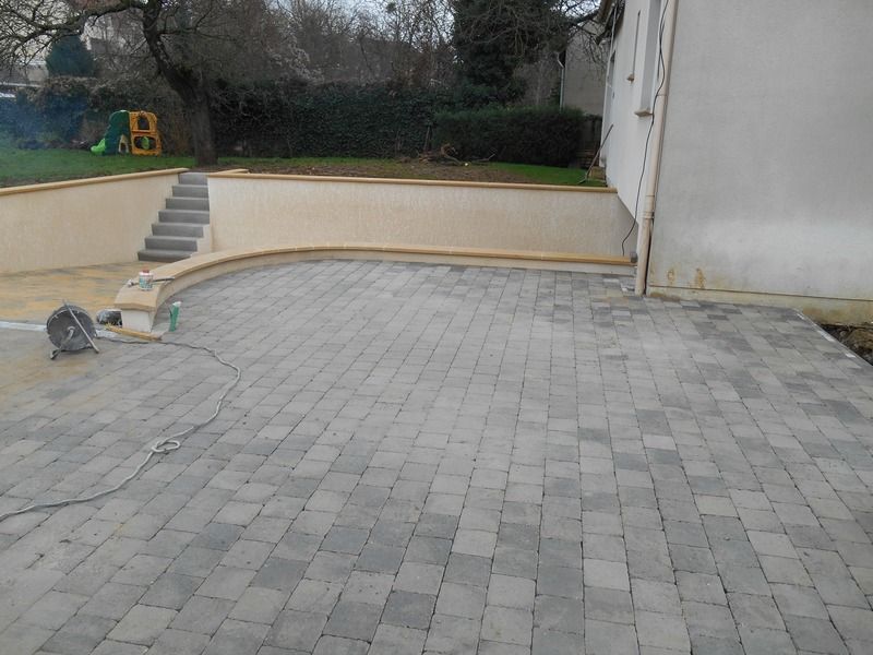Petite cour pavée avec des marches, un mur de soutènement incurvé et un chat près du côté gauche.