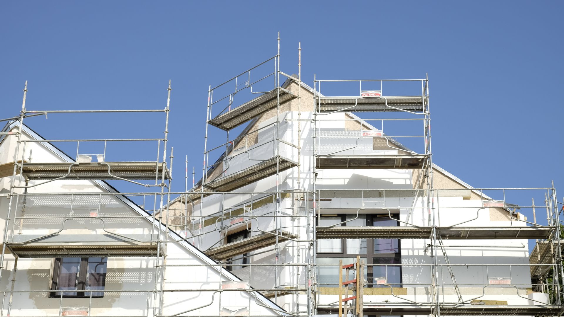Extérieur d'une maison en construction, échafaudages autour du toit et des murs, ciel bleu.