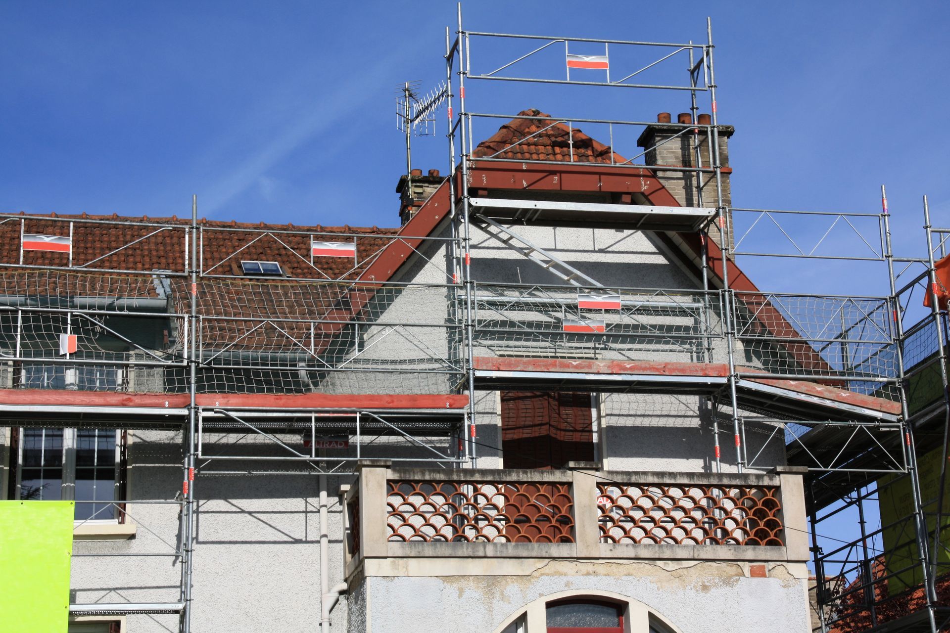 Un bâtiment avec des échafaudages, un toit de tuiles rouges et un ciel bleu.