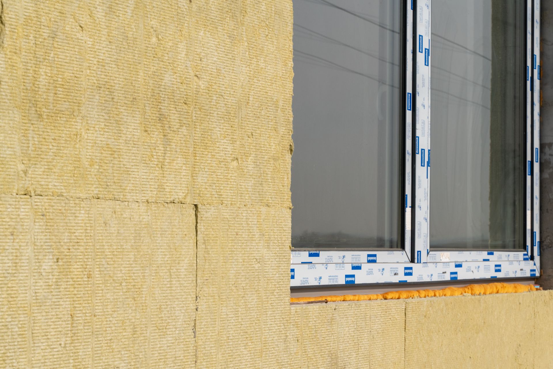 Mur extérieur isolé en jaune clair jouxtant une fenêtre à cadre blanc.