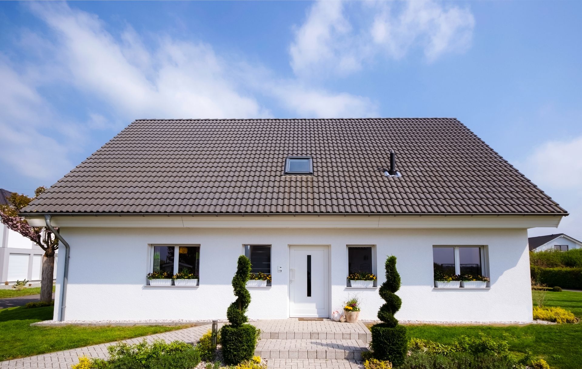 Maison blanche au toit gris, petites fenêtres, porte d'entrée et pelouse bien entretenue sous un ciel bleu.