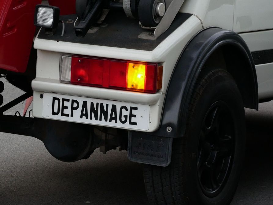 Véhicule de dépannage blanc avec des feux allumés et un panneau DÉPANNAGE à l'arrière.