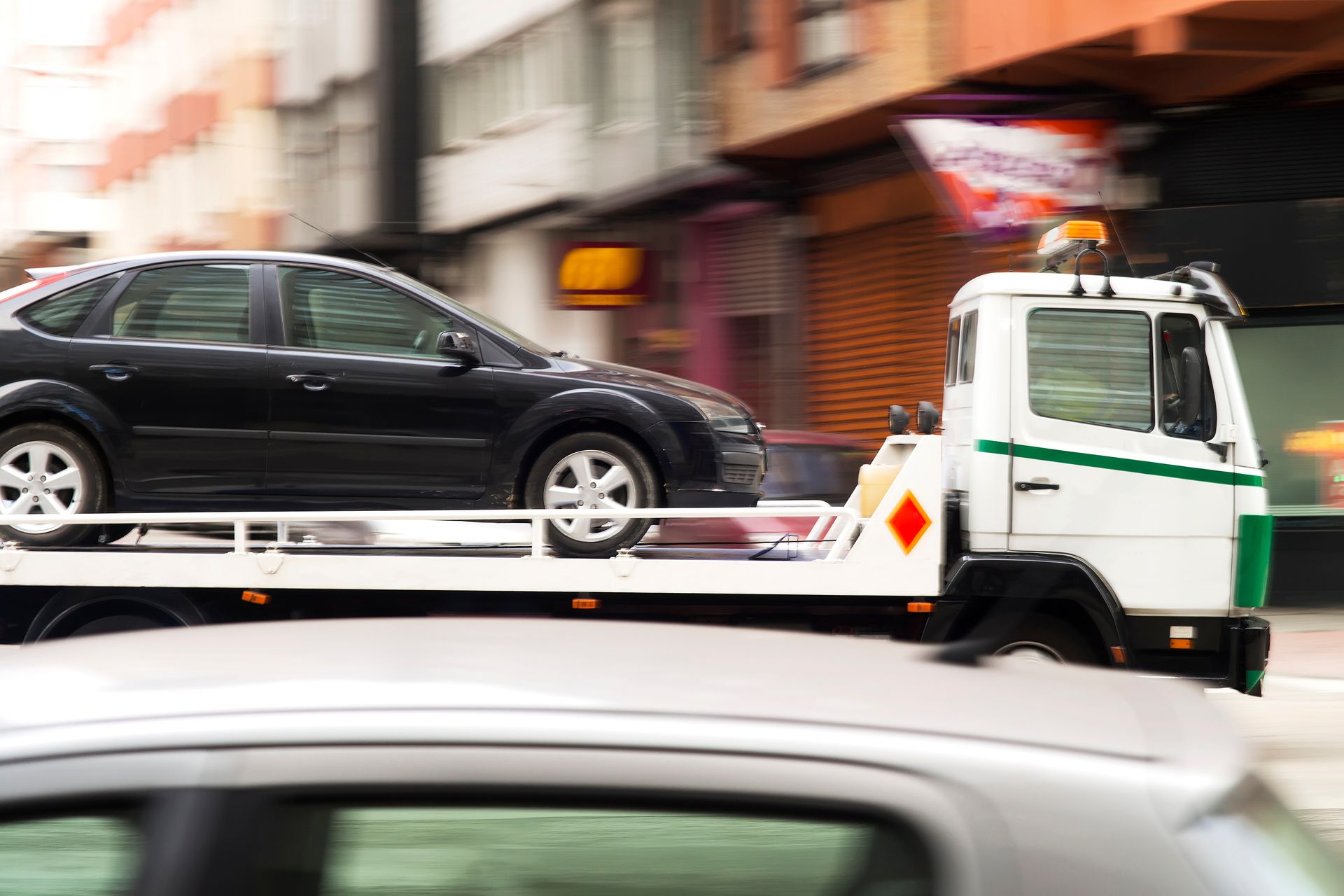 Un SUV noir sur une dépanneuse passe devant des bâtiments flous dans une rue de la ville.