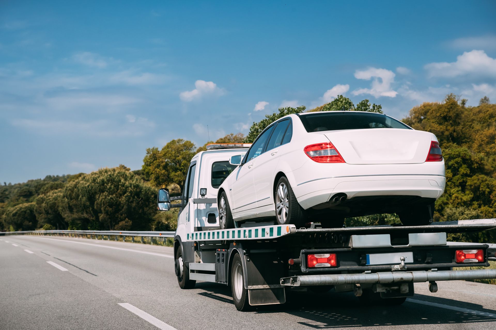 Une berline blanche sur une dépanneuse circulant sur une autoroute sous un ciel bleu.