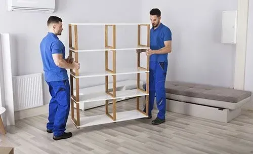 Dos trabajadores con uniformes azules ensamblan una estantería de madera en una habitación luminosa.