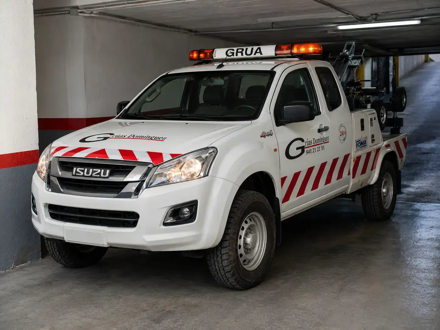 Camión de rescate Isuzu blanco con luces naranjas intermitentes estacionado en un garaje.