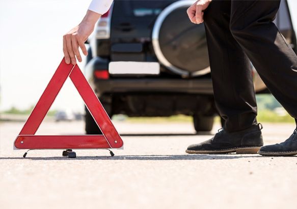 Un hombre sostiene un triángulo rojo de advertencia delante de un coche averiado.