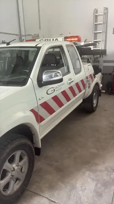 Camioneta blanca utilitaria con franjas diagonales rojas estacionada dentro de un garaje, escalera en la caja.