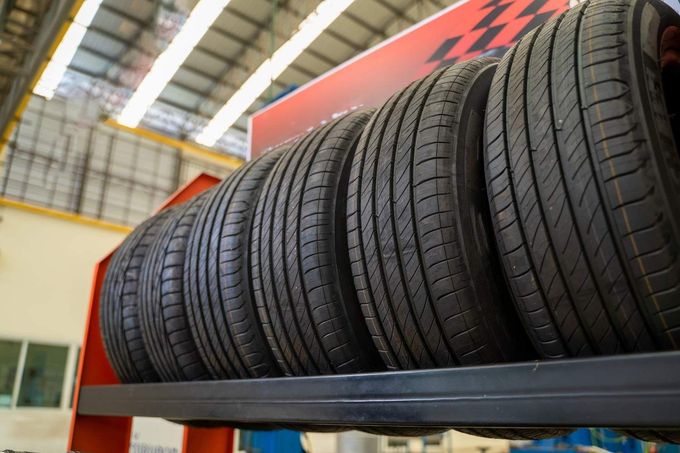 Neumáticos negros apilados en una estantería de un almacén, con una pancarta roja encima.