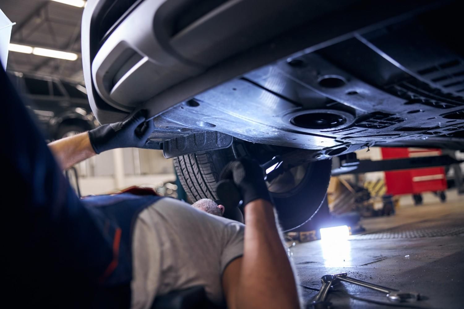 Mecánico trabajando debajo de un coche en un taller, utilizando herramientas cerca de los bajos del vehículo.