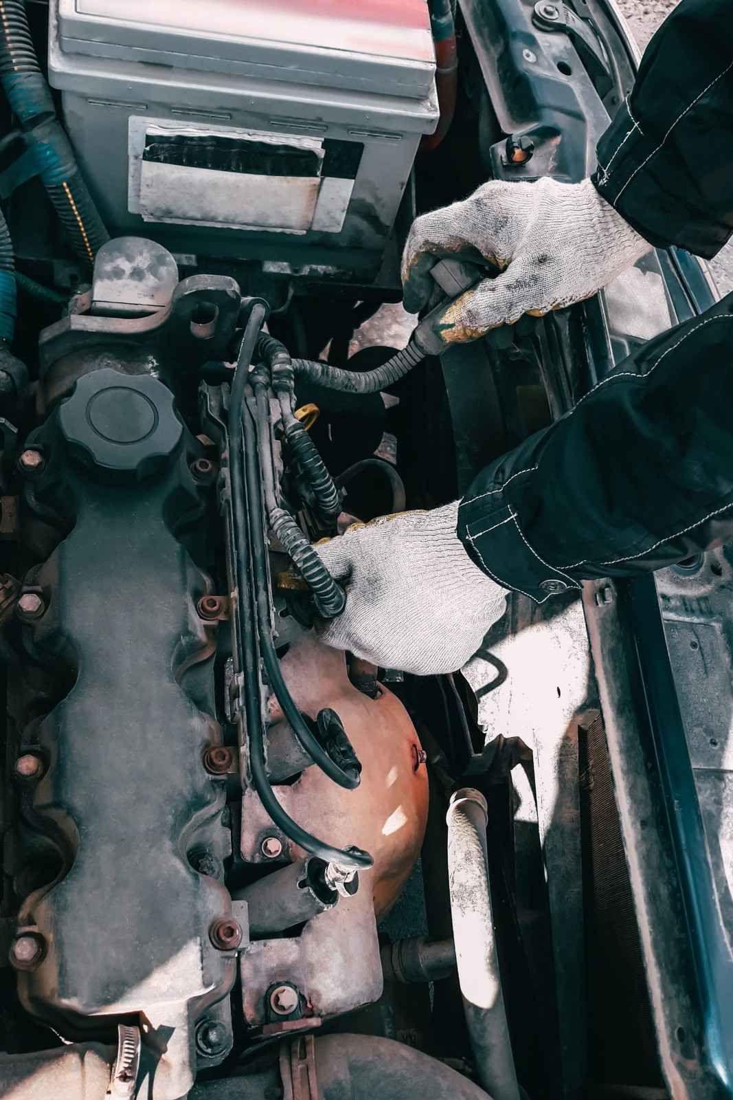 Mecánico con guantes blancos trabajando en el motor de un coche en un entorno nevado al aire libre.