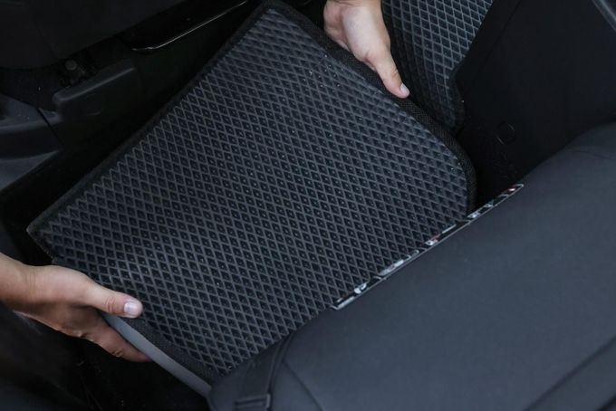 Manos levantando un cojín de asiento de coche de malla negra de entre dos asientos de coche.