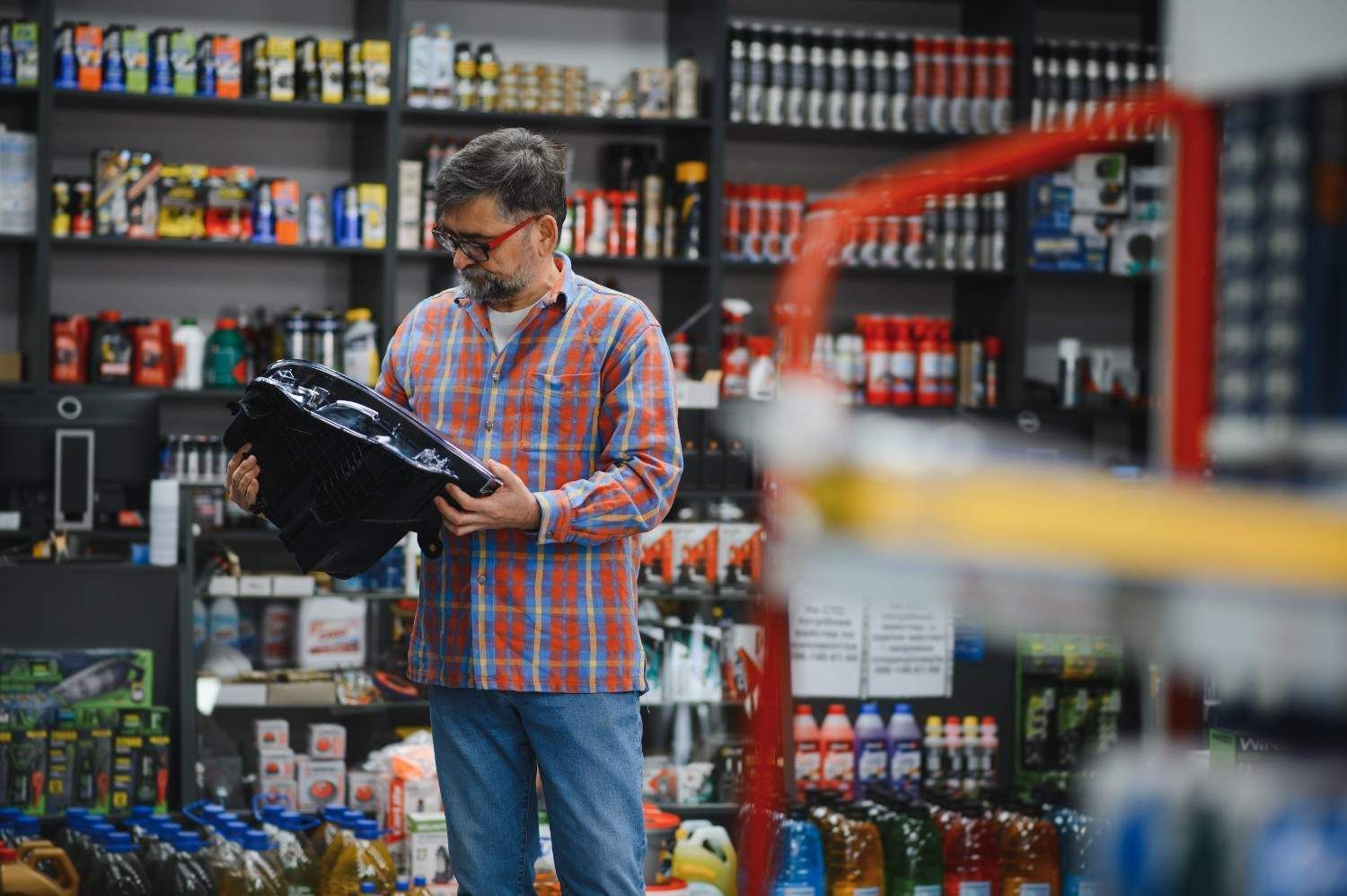 Un hombre con camisa a cuadros y mascarilla revisa una bolsa en un pasillo de una tienda con estantes de artículos para mascotas.
