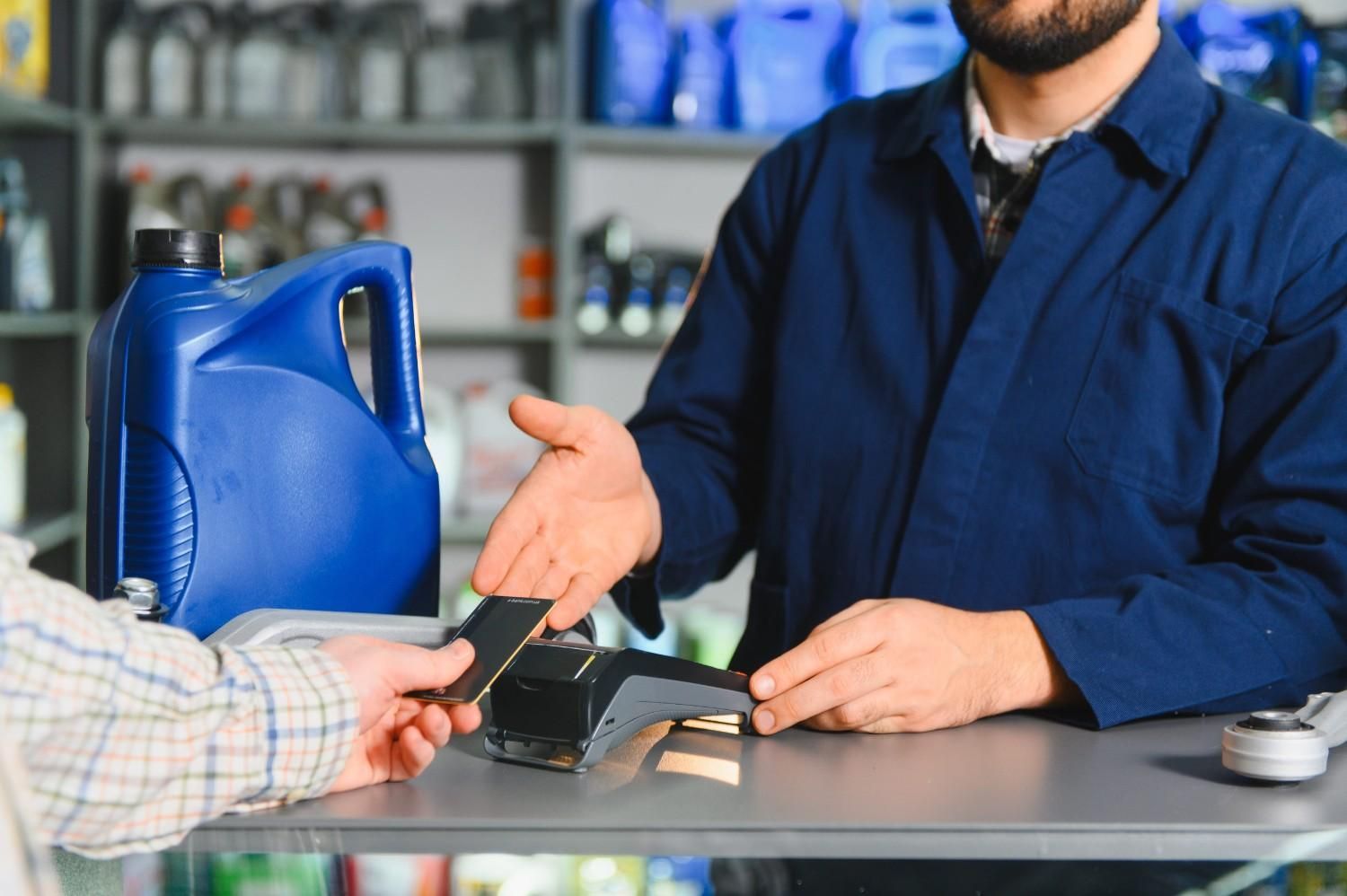 Un empleado en un mostrador le da el cambio a un cliente, con una lata de combustible azul cerca.