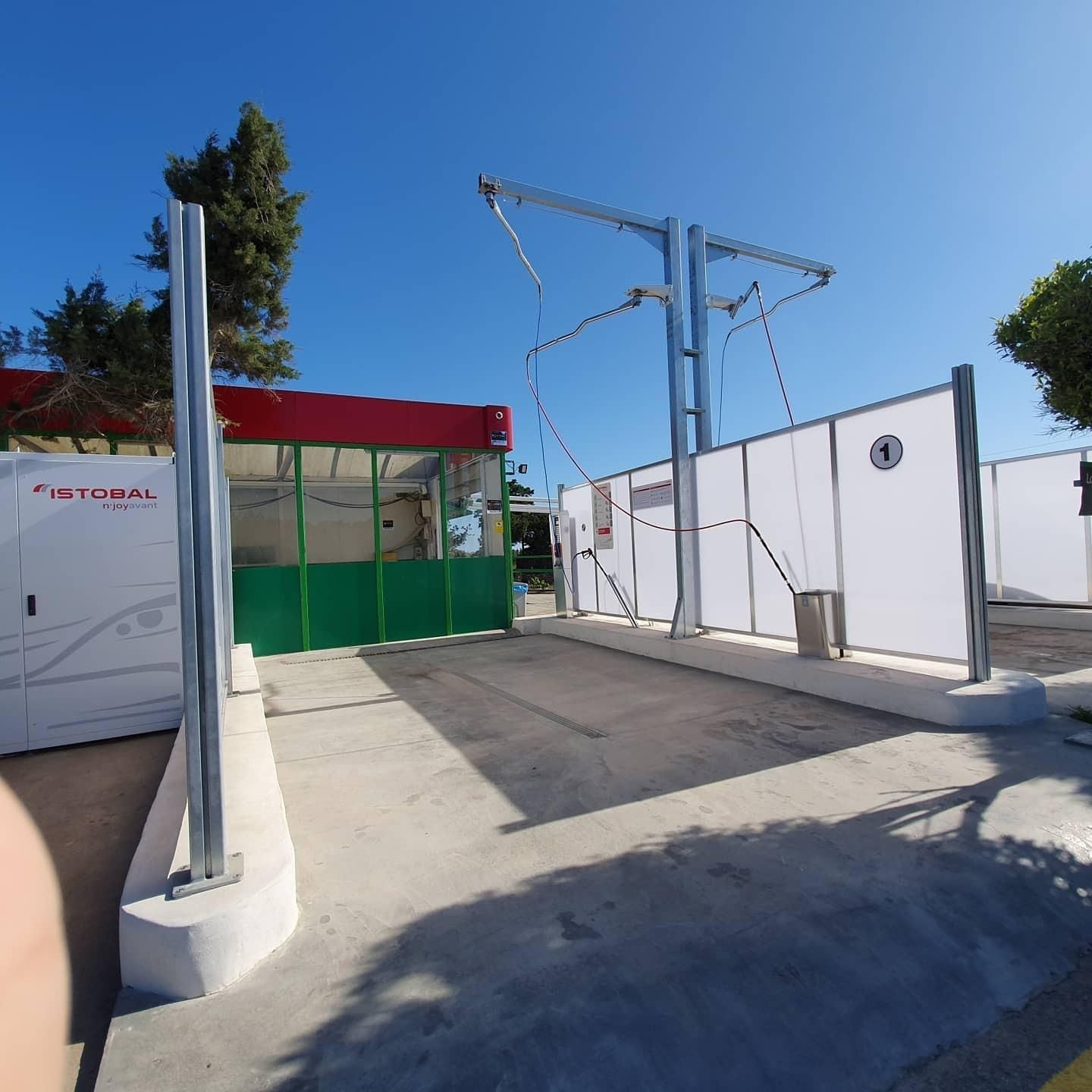 Puesto de control exterior soleado con paredes blancas, quiosco con techo rojo y líneas eléctricas aéreas.