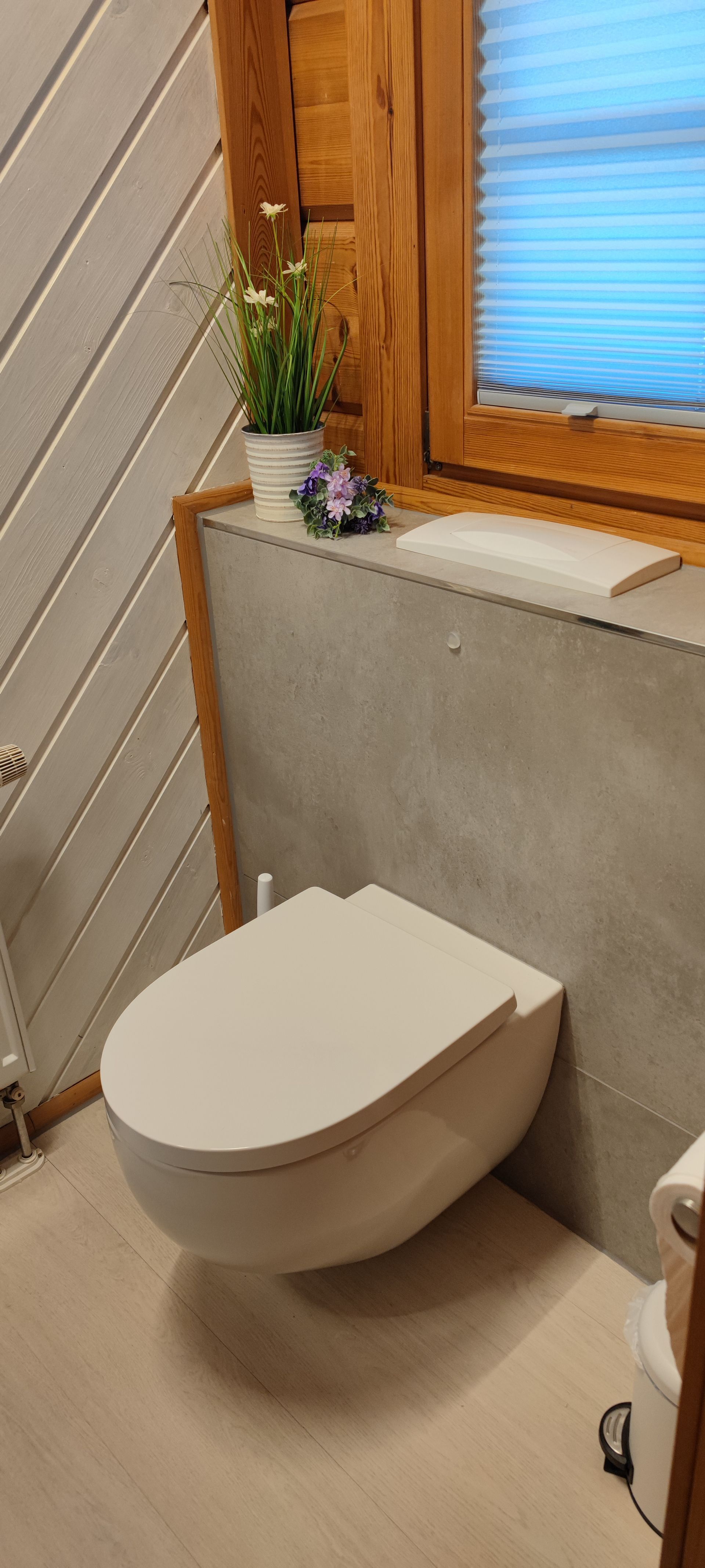 In einem Badezimmer ist eine Toilette neben einem Fenster an der Wand montiert.