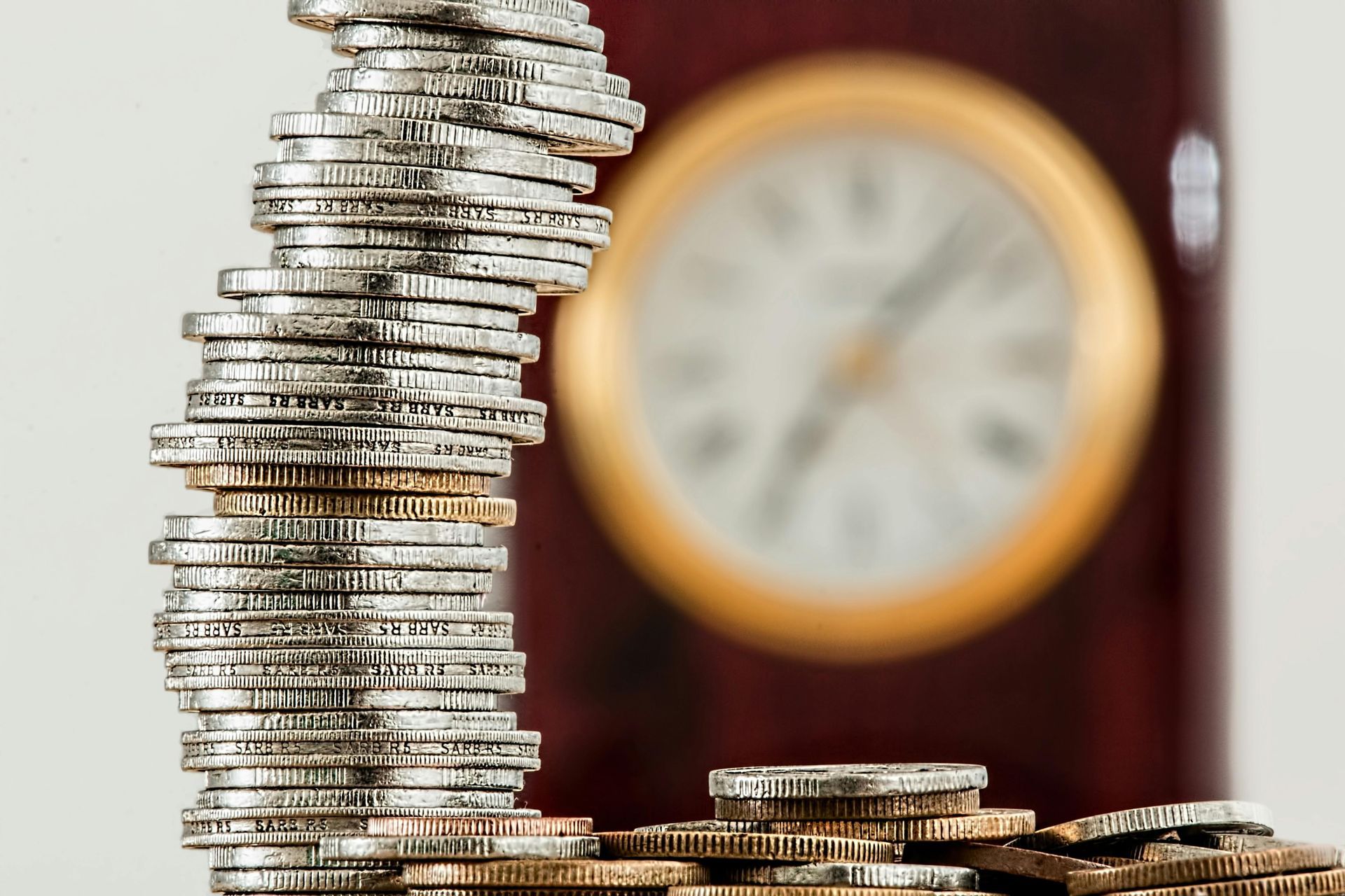 Des piles de pièces sur une table avec une horloge floue en arrière-plan