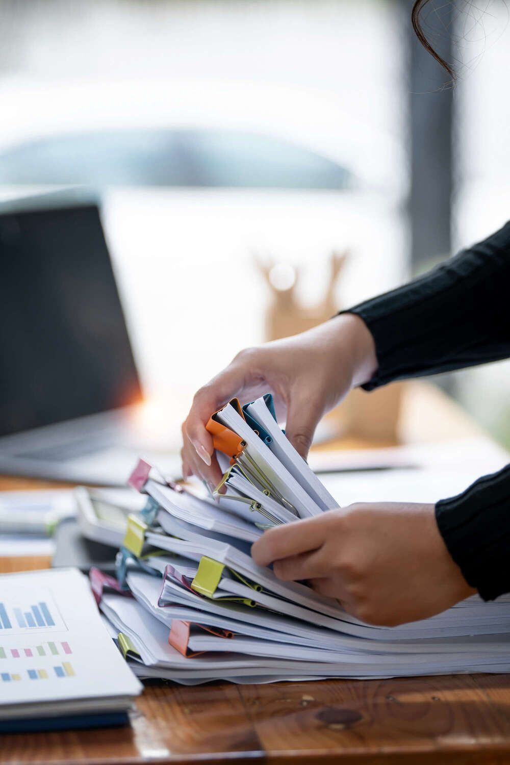 Mains triant une pile de papiers sur un bureau en bois à côté d’un ordinateur portable